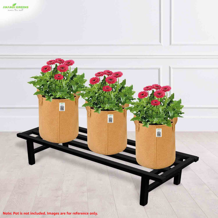 Three tan fabric pots with plants on a black metal stand against a white paneled wall.
