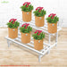 White metal plant stand with brown pots and red flowers against a white brick wall.