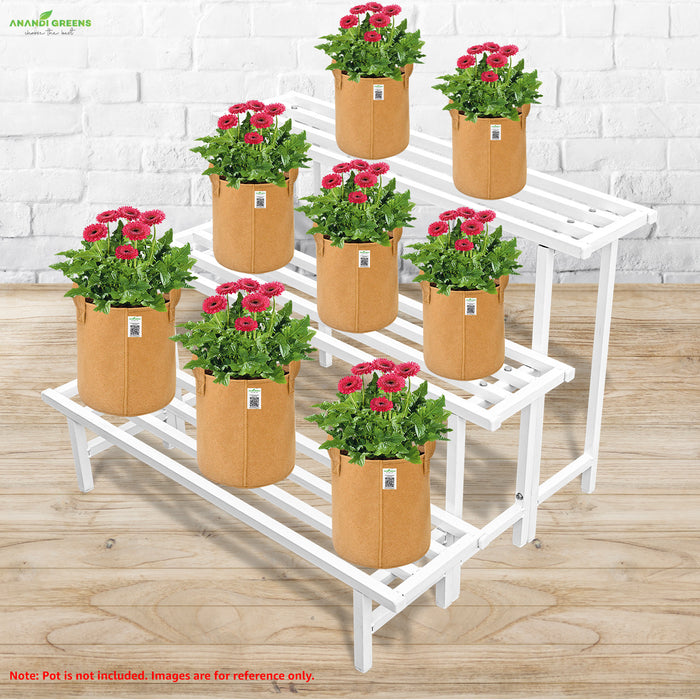 White metal plant stand with pots of flowers against a white brick wall.