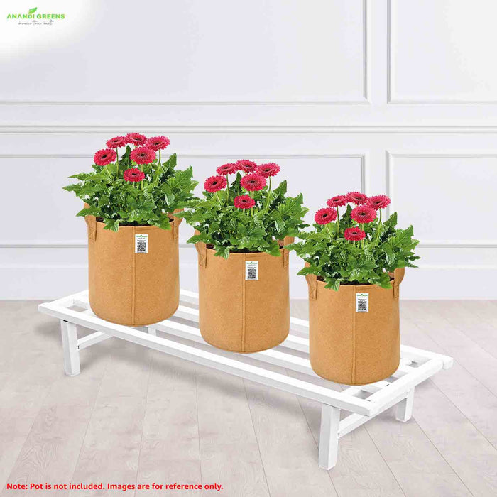 Three brown fabric pots with plants on a white stand against a light-colored wall.