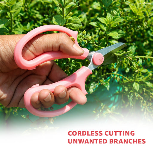 Hand holding pink garden shears with green foliage in the background
